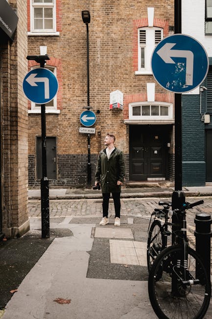 View looking out from under an archway onto a narrow cobblestone street lined with multi-storey Victorian-style brick buildings. Several parked cars are visible along the sides of the street, which features potted plants and small trees on the pavements. The scene is lit by natural daylight, creating a scene representative of urban residential street scenes typical of Clerkenwell. This setting may relate to house removals or moving services provided by Man with Van Clerkenwell, with potential for furniture transport or home relocation activities occurring nearby or within this area.